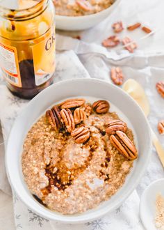 a bowl of oatmeal with pecans in it and a jar of honey on the side