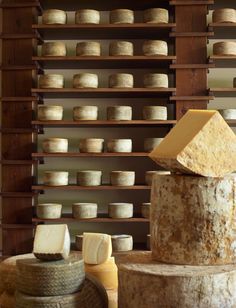 several different types of cheese on display in a room with wooden shelves and shelving