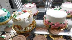 many different types of cakes on display in a glass case with frosting and sprinkles