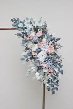 a bridal bouquet with blue and pink flowers on a wooden stand in front of a white wall