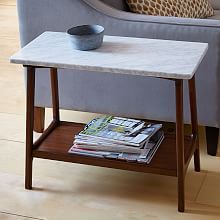 a table with magazines and a bowl on it in front of a gray couch next to a chair