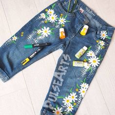 a pair of jean pants with flowers painted on them and pens in the back pocket