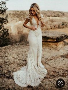 a woman standing on top of a rocky hillside wearing a wedding dress with an open back