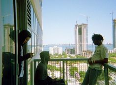 two young men standing on a balcony looking out at the city and buildings in the distance