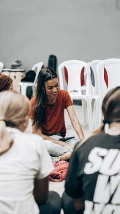 a group of people sitting on the ground in front of white chairs and one woman is smiling