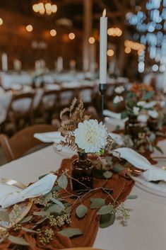 the table is set with white flowers and greenery, candlesticks and napkins