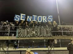 some fans are holding up signs in front of a fence at a football game with the words senior's back to black written on it