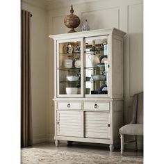 a white china cabinet with glass doors and drawers in a living room next to a chair