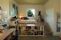 a room with a bed, bookshelf, desk and stairs leading to the second floor