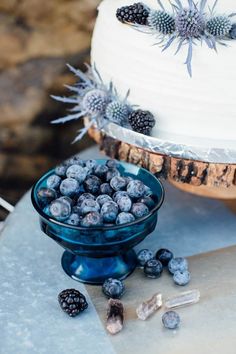 a white cake with blueberries in a bowl on a table next to other desserts