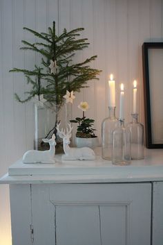 a white mantle with candles and glass bottles on it, next to a small christmas tree