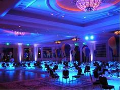 a banquet hall set up for a party with blue lights and balloons on the ceiling