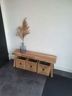 a wooden bench with three baskets underneath it and a plant in the corner next to it