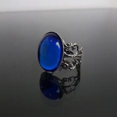 This ornate ring features a Sapphire blue cabochon (18 x 13 mm) on a stunning filigree band. The Sterling silver plated filigree ring is adjustable so one size fits all. The Sapphire blue cabochon catches the light beautifully. Nickel and lead free. The Bella ring is available in Black Onyx, Ruby red and Sapphire blue. This Bella Sapphire blue filigree ring perfectly complements many of our chokers. ***********************************************************Gift wrappingAll jewellery is beautifu Sapphire Victorian Rings For Gift, Blue Gothic Jewelry For Gift, Gothic Blue Metal Jewelry, Gothic Sapphire Jewelry, Blue Victorian Metal Jewelry, Goth Ring, Ornate Ring, Medieval Rings, Steampunk Rings