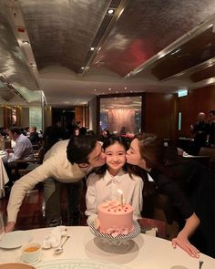 a man and woman kissing in front of a pink cake with candles on it at a restaurant