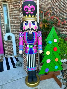 a nutcracker standing next to a christmas tree in front of a brick house