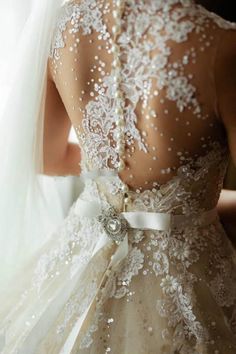 the back of a bride's wedding dress with white lace and pearls on it