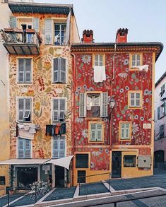 an apartment building with painted flowers on the side and windows above it, in front of other buildings