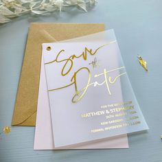 a white and gold save the date card next to some confetti on a table