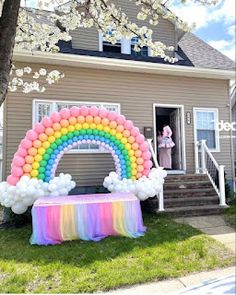 a rainbow balloon arch in front of a house with balloons on the top and below it