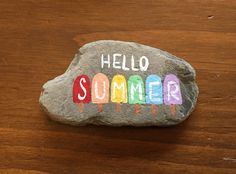 a rock with the word hello summer painted on it sitting on top of a wooden table