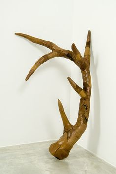 a wooden sculpture sitting on top of a cement floor next to a white walled wall