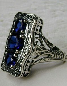 "Simulated Blue Sapphire Ring 3Stone Rectangle#60 Custom Made This is a lovely late Victorian era reproduction ring in solid sterling silver. The gorgeous filigree ring is set with 3 round-cut simulated blue sapphire gemstones. The 2 smaller blue sapphire gems are 4.5mm in diameter, and the center one is 6mm in diameter. This filigree setting is a casting from an actual Antique ring; notice the amazing etched band... The ring sits 3/4th\" (19mm) NS on the finger. The quality of the silver and ge Silver Rectangular Sapphire Ring, Classic Silver Rectangular Sapphire Ring, Elegant Three Stone Crystal Ring For Formal Occasions, Elegant Sapphire Ring With Rectangular Accent Stones, Elegant Formal Three Stone Crystal Ring, Elegant Formal Three-stone Crystal Ring, Art Deco Sterling Silver Sapphire Promise Ring, Blue Multi-stone Sapphire Ring In Art Deco Style, Vintage Sapphire Three-stone Ring