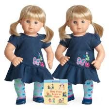 two dolls standing next to each other in front of a box with a book on it