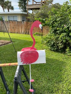 a pink flamingo standing on top of a white box in the grass next to a fence