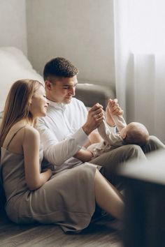 a man and woman are sitting on the floor with a baby in their lap looking at each other