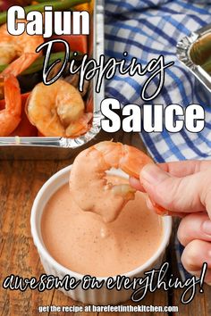 a person dipping sauce into a bowl with shrimp in the background and text saying cajun dipping sauce