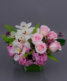 a vase filled with pink and white flowers on top of a gray table next to green leaves