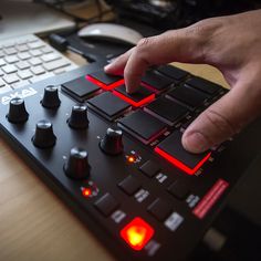 a hand is pressing buttons on an electronic device that sits on a desk next to a keyboard