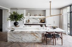 a kitchen with marble counter tops and wooden flooring in the center, surrounded by black chairs