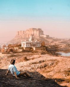 a man sitting on top of a rock next to a large castle in the distance