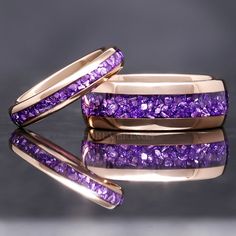 two gold rings with purple stones on them sitting on a reflective surface next to each other