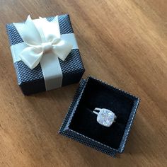 an open box with a ring inside on a wooden table next to a white bow