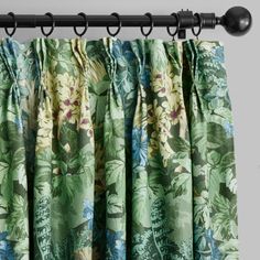 the curtain is open and has green flowers on it, with black metal rods hanging from the rod