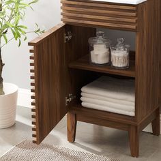 a wooden cabinet with towels on it and a potted plant in the corner next to it