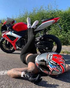 a woman laying on the ground next to a red motorcycle and wearing black tights