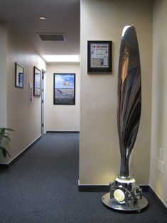 an office hallway with a large metal sculpture on the floor and framed pictures on the wall