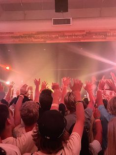 a large group of people at a concert with their hands in the air and lights on