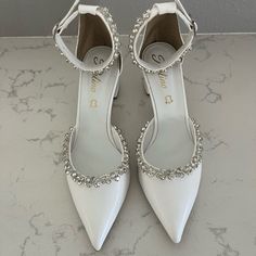 a pair of white high heeled shoes with crystal embellishments on the toes