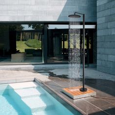 an outdoor swimming pool with water spouting from it's side, next to a stone building