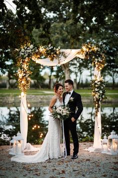 a bride and groom standing under an arch with candles