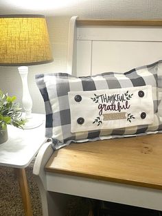 a pillow sitting on top of a wooden bench next to a lamp and potted plant