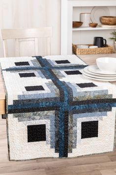 a quilted table runner on top of a wooden dining room table with plates and bowls