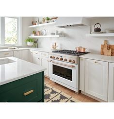 a kitchen with white cabinets and green counter tops, an oven in the center is surrounded by open shelving