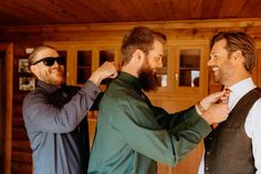 two men helping another man put on his tie