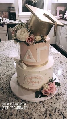 a three tiered cake decorated with flowers and a graduation cap on top is sitting on a kitchen counter